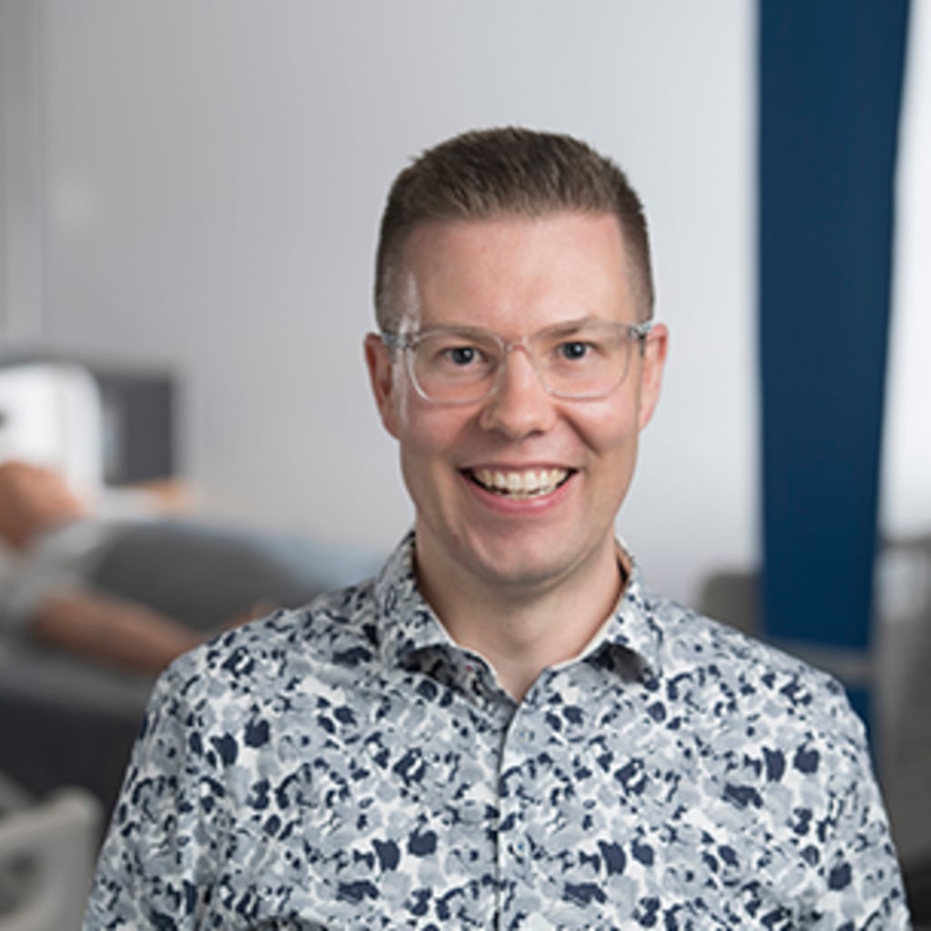 A smiling man in a floral shirt stands in a research setting related to early-onset bowel cancer centre of research excellence.