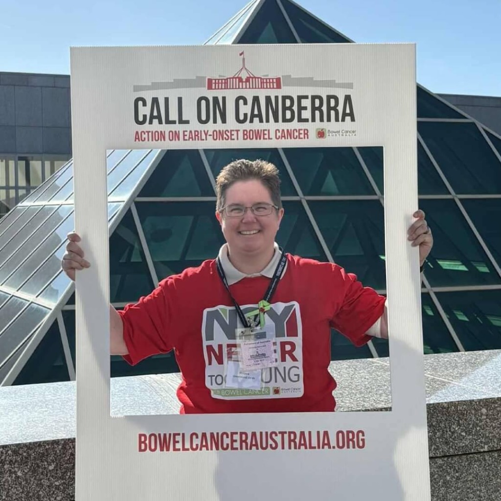 A person in a red shirt holds a frame that reads "Call on Canberra" outside, advocating for early-onset bowel cancer.
