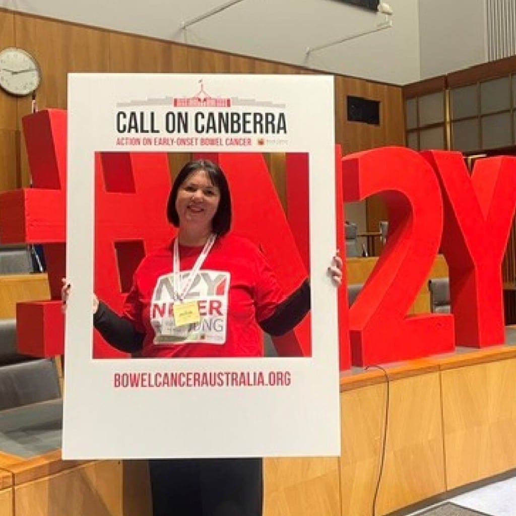 A woman holds a frame with "Call on Canberra" and "Action on early-onset bowel cancer" in a conference room.