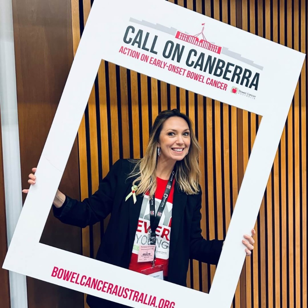A woman holds a frame with "Call on Canberra" and "Action on early-onset bowel cancer" at an advocacy event.