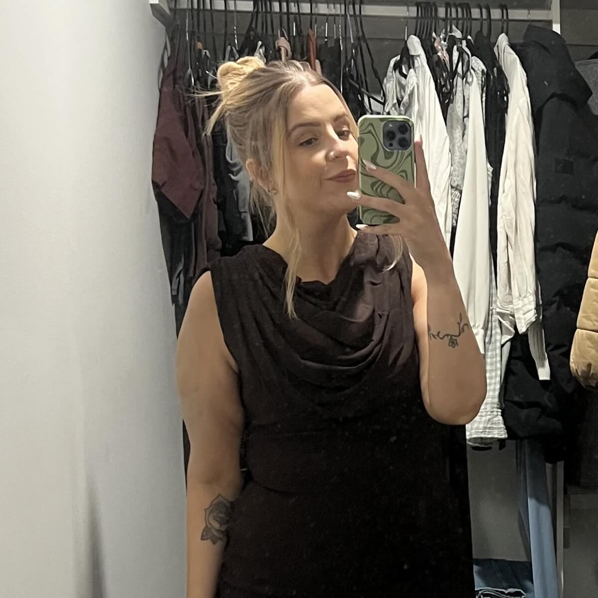 A woman with blonde hair in a bun takes a selfie in a closet with various clothes hanging in the background.