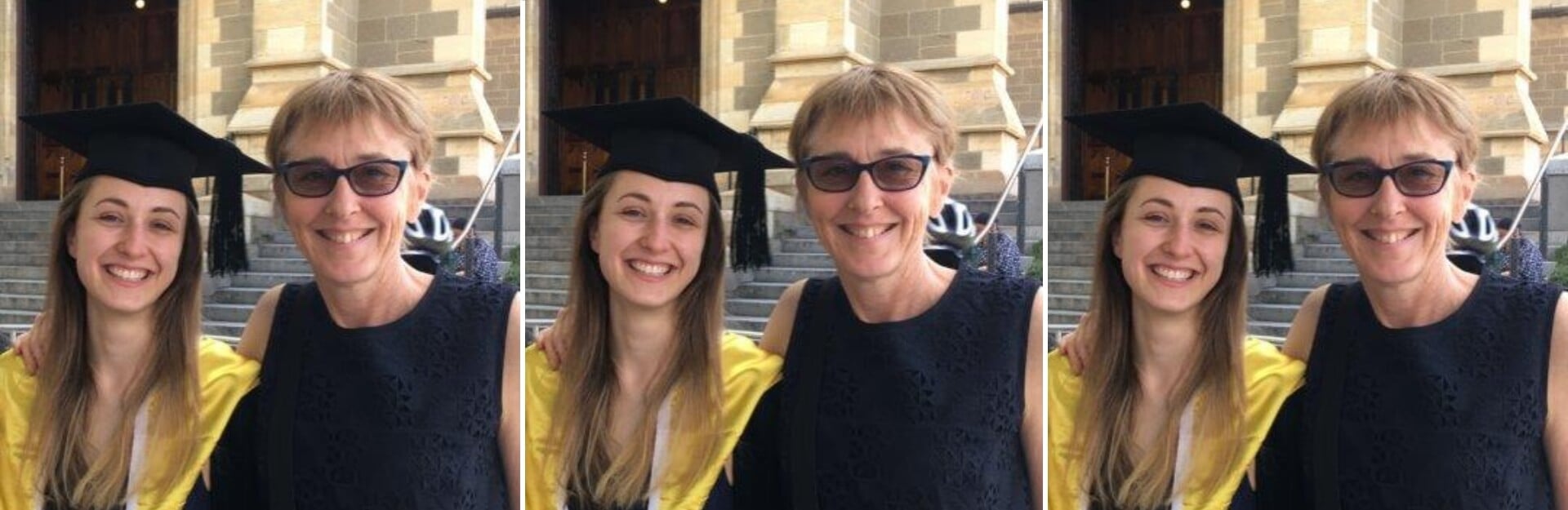 Two women smile for a photo outside a building. One wears a graduation cap and gown, while the other wears a dark dress.