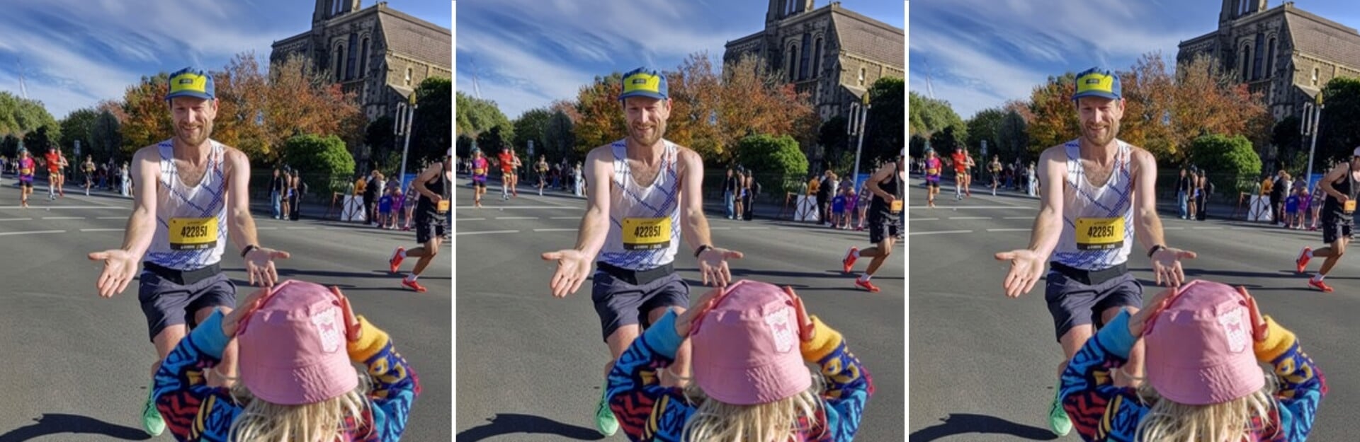 A runner reaches out to a child in a pink hat during the Sydney Marathon, with spectators and trees in the background.