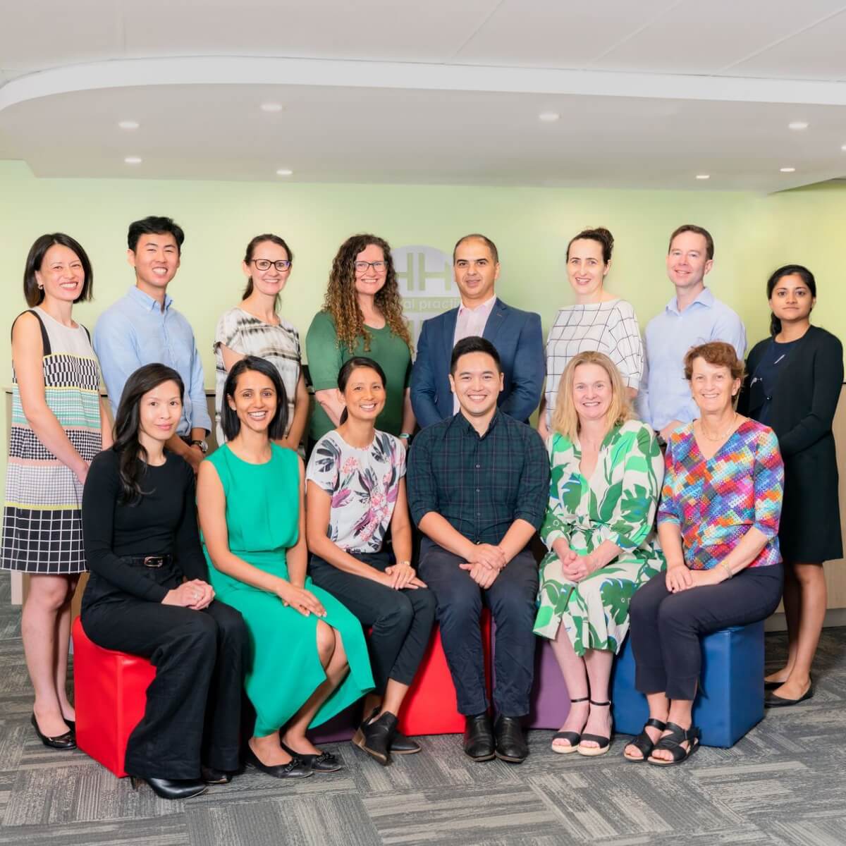 A diverse group of healthcare professionals poses together in a brightly lit office, some seated on colorful cubes.