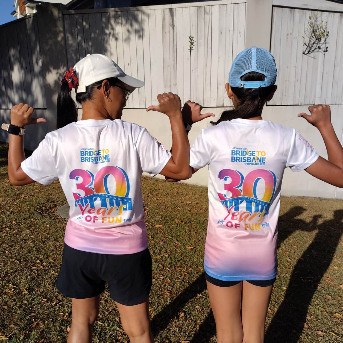 Two people wearing matching white shirts with colorful text celebrating "30 Years of Fun" for the Bridge to Brisbane event.